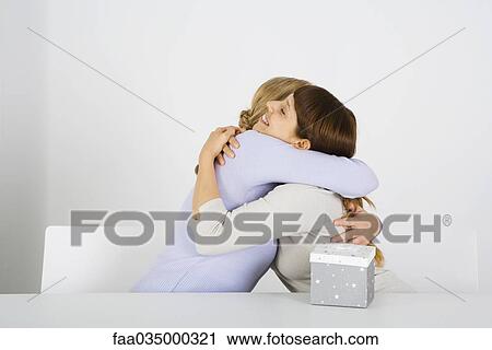 Women embracing, gift on table nearby View Large Photo Image Stock Image - Women embracing, gift on table nearby. Fotosearch