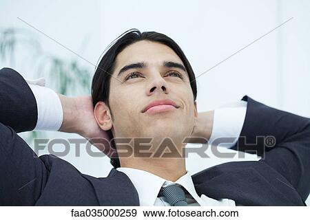 Young businessman leaning back with hands behind head, looking up, portrait View Large Photo Image Stock Photo - Young businessman leaning back with hands behind head, looking up, portrait. Fotosearch