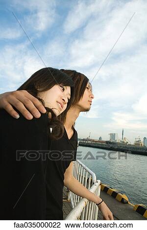 Young couple standing on harbor, looking at view View Large Photo Image Stock Image - Young couple standing on harbor, looking at view. Fotosearch