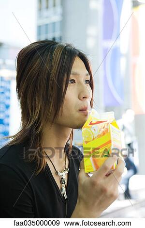 Stock Photo - Young Japanese man drinking from juice carton. Fotosearch