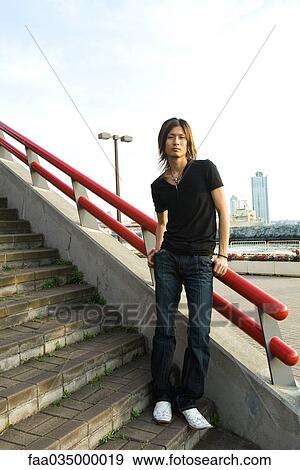 Young Japanese man standing on stairs, leaning against railing, portrait View Large Photo Image Stock Photo - Young Japanese man standing on stairs, leaning against railing, portrait. Fotosearch