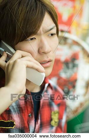 Young man talking on cell phone, furrowing brow View Large Photo Image Picture - Young man talking on cell phone, furrowing brow. Fotosearch