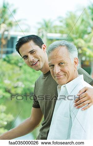 Young man with arm around father's shoulder, both smiling, portrait View Large Photo Image Stock Photograph - Young man with arm around father's shoulder, both smiling, portrait. Fotosearch