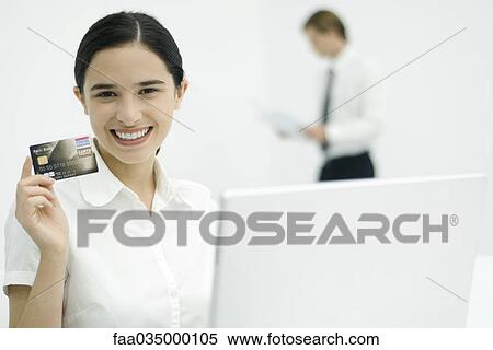 Young woman holding up credit card, smiling at camera View Large Photo Image Stock Photography - Young woman holding up credit card, smiling at camera. Fotosearch