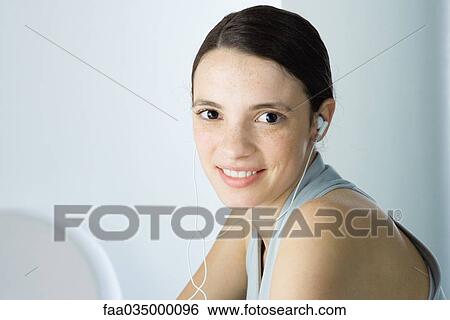 Stock Photograph - Young woman listening to earphones, smiling at camera. Fotosearch