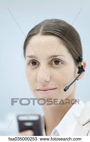 Stock Image - Young woman wearing headset, smiling, portrait. Fotosearch