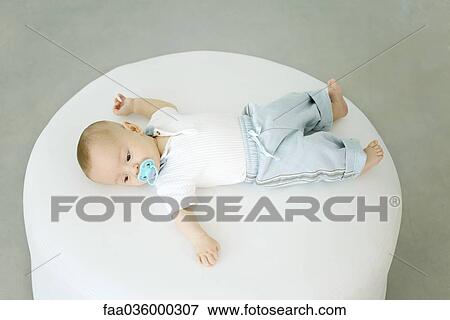 Baby lying on ottoman, sucking on pacifier, high angle view View Large Photo Image Stock Photo - Baby lying on ottoman, sucking on pacifier, high angle view. Fotosearch