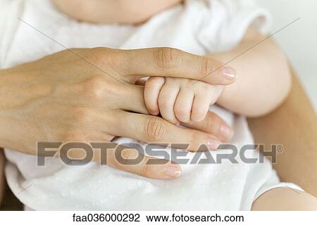 Stock Image - Baby's hand holding adult's finger, close-up. Fotosearch