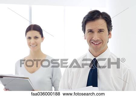 Business colleagues standing, smiling at camera, woman holding documents View Large Photo Image Stock Photo - Business colleagues standing, smiling at camera, woman holding documents. Fotosearch