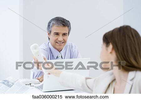 Businessman handing female associate telephone View Large Photo Image Stock Photography - Businessman handing female associate telephone. Fotosearch
