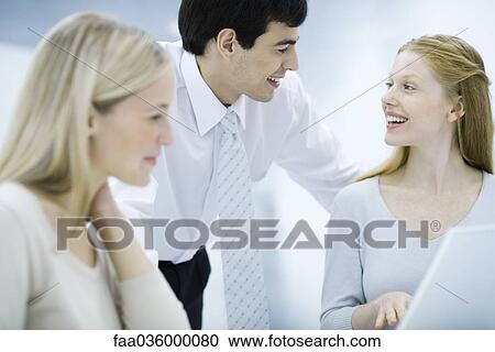 Businessman leaning over, chatting with female colleagues View Large Photo Image Stock Image - Businessman leaning over, chatting with female colleagues. Fotosearch