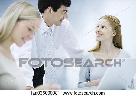 Businessman leaning over, chatting with female colleagues View Large Photo Image Stock Image - Businessman leaning over, chatting with female colleagues. Fotosearch