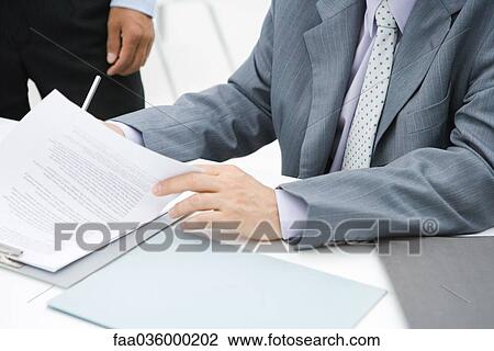Businessman reviewing document at desk, cropped view View Large Photo Image Stock Image - Businessman reviewing document at desk, cropped view. Fotosearch