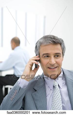 Stock Image - Businessman using cell phone in office. Fotosearch