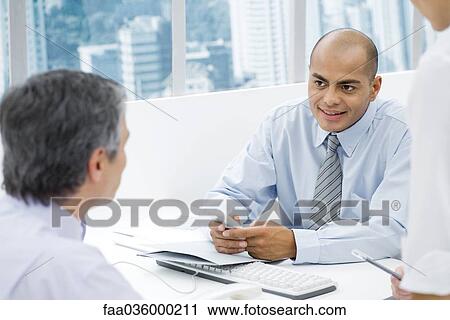 Stock Image - Businessmen having a meeting at desk, focus on man in background. Fotosearch
