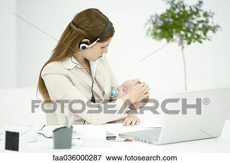 Businesswoman in office, holding sleeping baby, using headset View Large Photo Image Stock Photo - Businesswoman in office, holding sleeping baby, using headset. Fotosearch