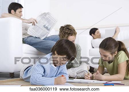 Stock Photo - Children coloring on the floor in living room, parents reading in background. Fotosearch