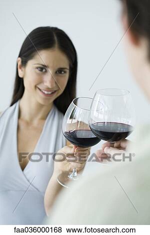 Stock Photo - Couple clinking glasses of red wine, woman smiling at camera, cropped view. Fotosearch
