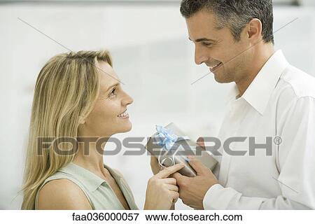 Couple exchanging gift, smiling at each other, side view View Large Photo Image Stock Photo - Couple exchanging gift, smiling at each other, side view. Fotosearch