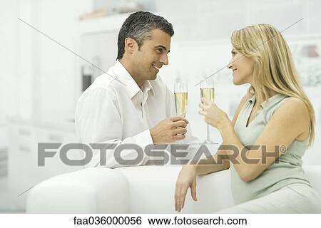 Stock Photograph - Couple holding champagne glasses, smiling at each other. Fotosearch