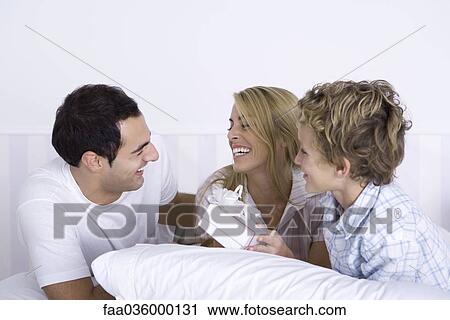 Family lying in bed together, woman holding gift View Large Photo Image Stock Image - Family lying in bed together, woman holding gift. Fotosearch