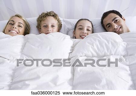 Family lying together in bed beneath comforter, smiling at camera View Large Photo Image Stock Photography - Family lying together in bed beneath comforter, smiling at camera. Fotosearch