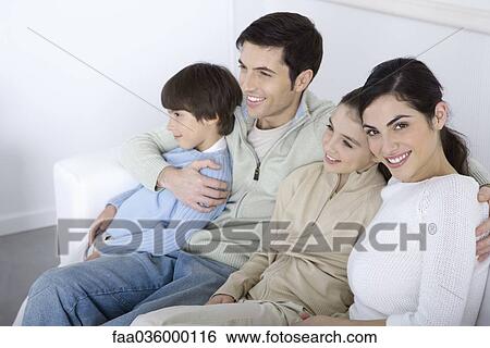 Stock Photograph - Family sitting together on sofa, looking away, woman smiling at camera. Fotosearch