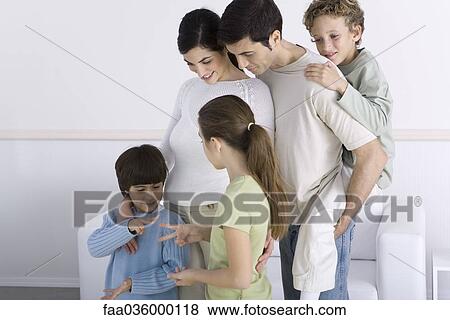 Stock Photo - Family standing together, watching son and daughter play "rock paper scissors". Fotosearch
