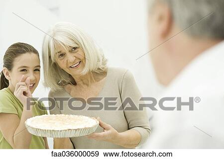 Grandmother and granddaughter offering pie to man in foreground, smiling View Large Photo Image Stock Photo - Grandmother and granddaughter offering pie to man in foreground, smiling. Fotosearch