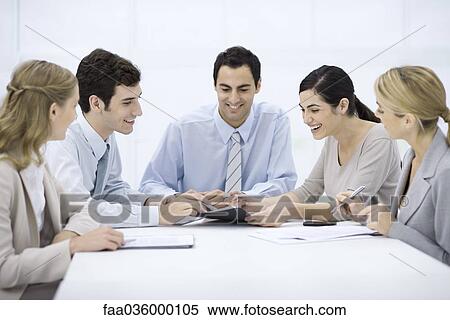 Stock Photography - Group of professionals sitting at table, discussing document. Fotosearch