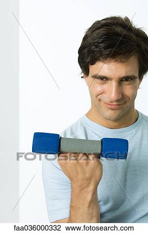 Stock Image - Man lifting dumbbell, smirking at camera. Fotosearch