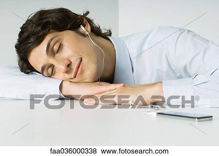 Man listening to MP3 player, resting head on arms, eyes closed View Large Photo Image Stock Photo - Man listening to MP3 player, resting head on arms, eyes closed. Fotosearch