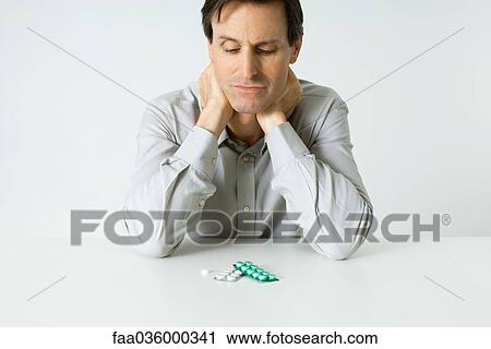 Man sitting next to pills, holding neck, looking down View Large Photo Image Stock Image - Man sitting next to pills, holding neck, looking down. Fotosearch