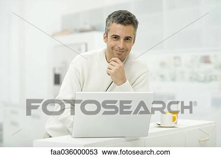 Man using laptop computer in kitchen, smiling at camera View Large Photo Image Stock Image - Man using laptop computer in kitchen, smiling at camera. Fotosearch
