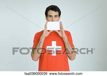 Man wearing Swiss flag tee-shirt, holding blank card in front of mouth View Large Photo Image Stock Photo - Man wearing Swiss flag tee-shirt, holding blank card in front of mouth. Fotosearch