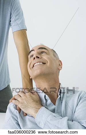 Stock Photograph - Mature man holding son's hand on shoulder, smiling up over shoulder, cropped view. Fotosearch