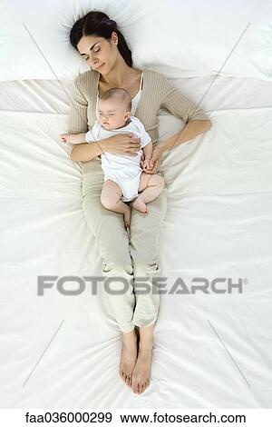 Stock Photo - Mother and baby napping together on bed, overhead view. Fotosearch
