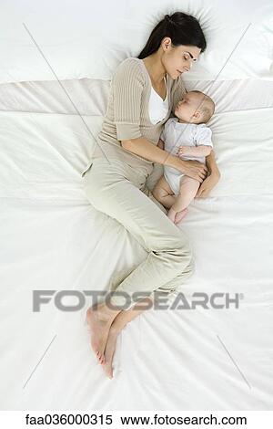 Stock Photography - Mother and baby sleeping on bed, overhead view. Fotosearch
