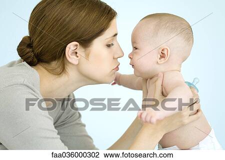 Stock Image - Mother holding baby up close to face, both smiling at each other. Fotosearch