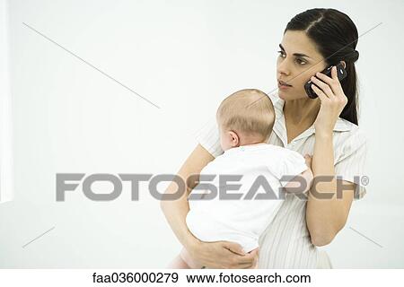 Mother holding infant, using cell phone View Large Photo Image Stock Photo - Mother holding infant, using cell phone. Fotosearch