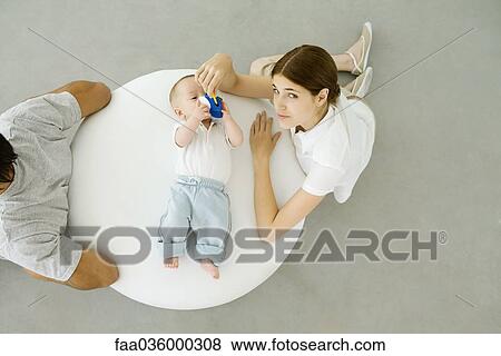 Mother playing with infant lying on ottoman, father sitting with back turned to them, overhead view View Large Photo Image Stock Photo - Mother playing with infant lying on ottoman, father sitting with back turned to them, overhead view. Fotosearch