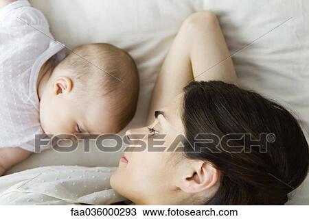 Stock Image - Mother watching baby napping, lying together on bed. Fotosearch