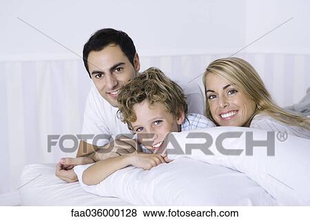 Parents and son lying on bed, smiling at camera, portrait View Large Photo Image Stock Photo - Parents and son lying on bed, smiling at camera, portrait. Fotosearch