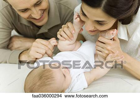 Parents smiling down at baby, mother holding baby's feet, cropped view View Large Photo Image Picture - Parents smiling down at baby, mother holding baby's feet, cropped view. Fotosearch