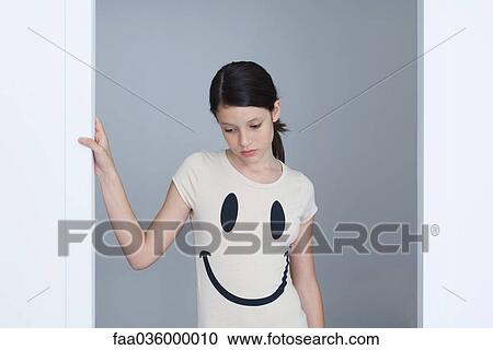 Stock Image - Preteen girl wearing smiley face tee-shirt, frowning, looking down. Fotosearch