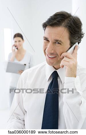 Professional man using cell phone, smiling at camera, woman on phone in background View Large Photo Image Stock Photo - Professional man using cell phone, smiling at camera, woman on phone in background. Fotosearch