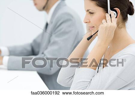 Professional woman adjusting headset, male colleague in background, side view View Large Photo Image Stock Image - Professional woman adjusting headset, male colleague in background, side view. Fotosearch
