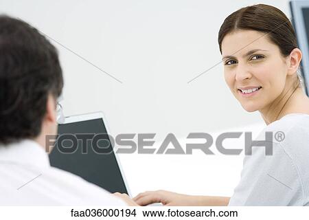 Professional woman in office, smiling over shoulder at camera View Large Photo Image Picture - Professional woman in office, smiling over shoulder at camera. Fotosearch