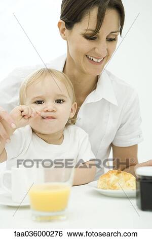 Professional woman sitting at breakfast table, toddler sitting on lap, spoon in mouth View Large Photo Image Stock Photograph - Professional woman sitting at breakfast table, toddler sitting on lap, spoon in mouth. Fotosearch