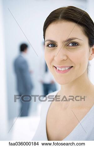 Professional woman smiling at camera, male colleagues in background View Large Photo Image Picture - Professional woman smiling at camera, male colleagues in background. Fotosearch